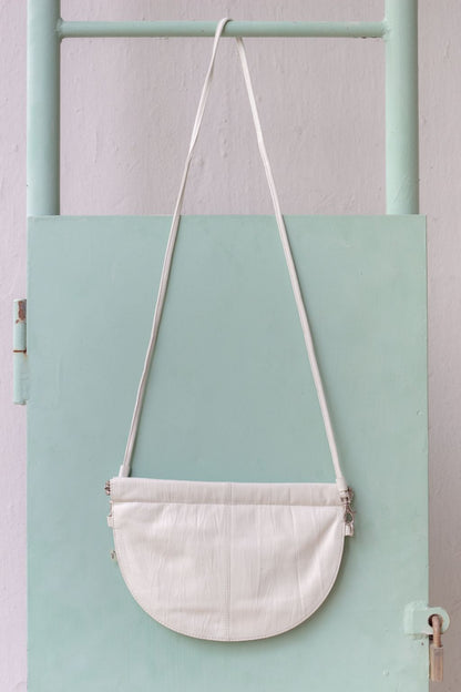 half moon crossbody bag in white in front of mint wall