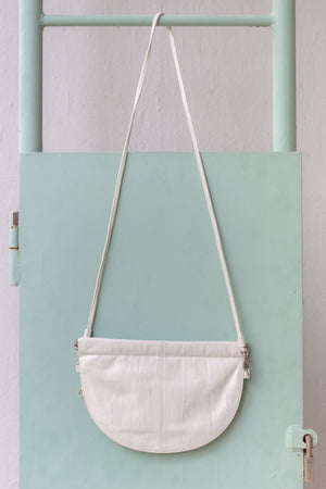 half moon crossbody bag in white in front of mint wall