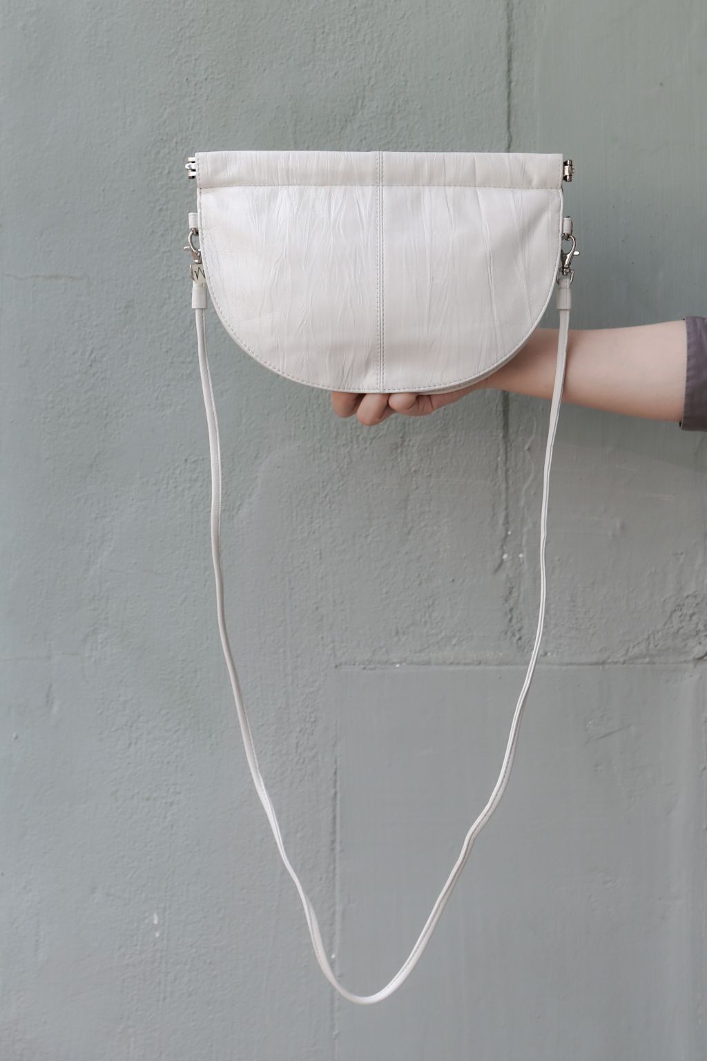 half moon crossbody bag in white  in front of grey wall