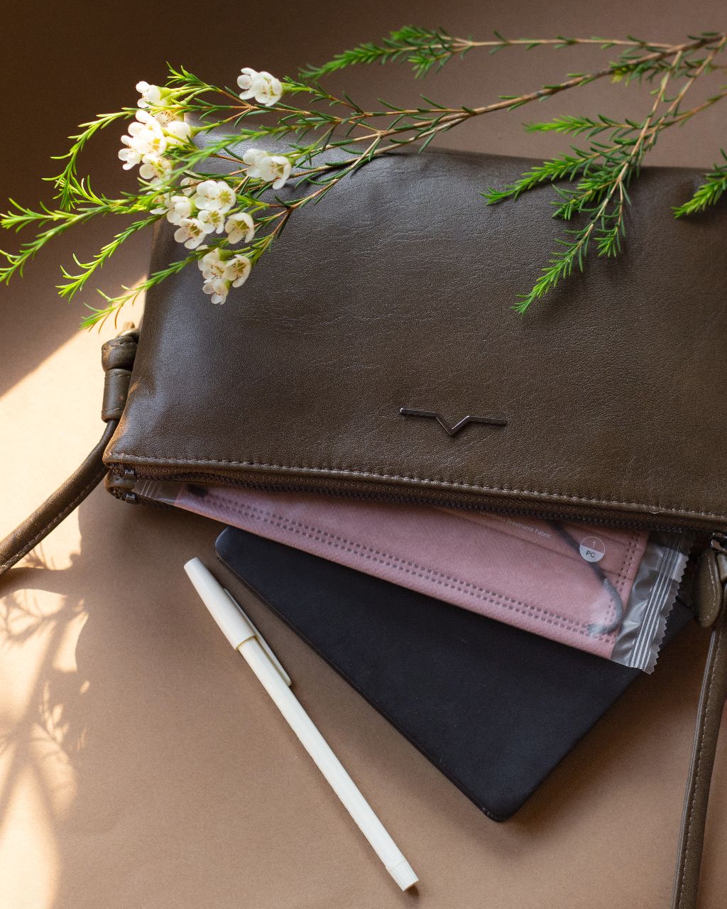 double zip rectangular crossbody in leather with face mask , note book and ball pens under natural lights