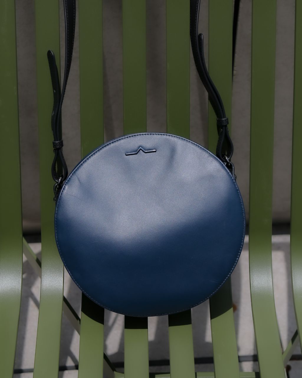 navy round crossbody leather bag on green chair